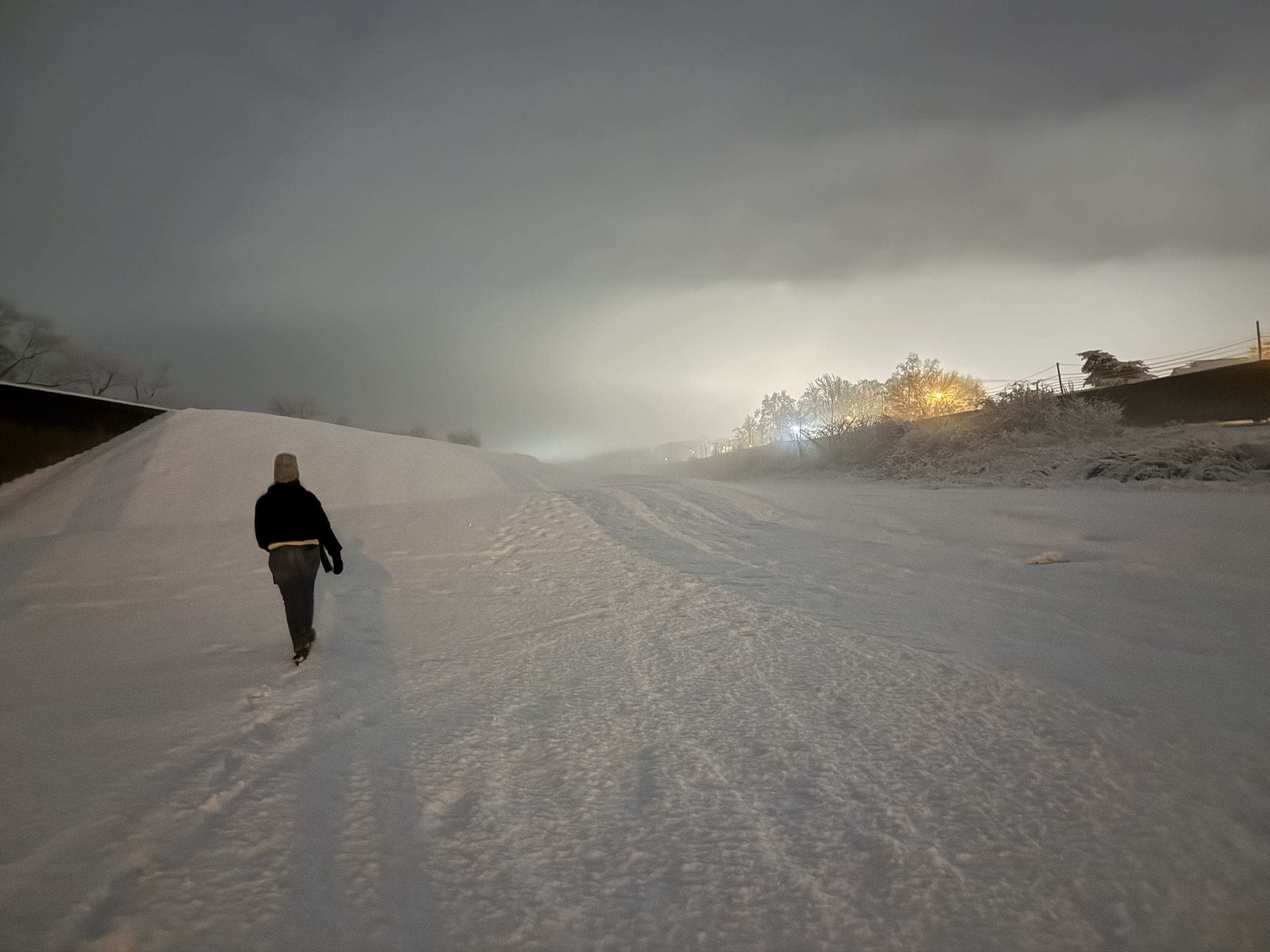 A person walks through a snowy landscape at night, illuminated by soft lights, evoking solitude and tranquility.