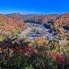 Autumn landscape with vibrant foliage, winding road, and a serene settlement under a clear blue sky invites tranquility and reflection.