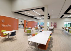 Bright, modern café interior with orange wall, white tables, colorful chairs, and ample natural light, fostering a lively atmosphere.