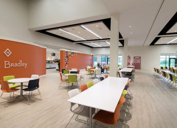 Bright, modern café interior with orange wall, white tables, colorful chairs, and ample natural light, fostering a lively atmosphere.