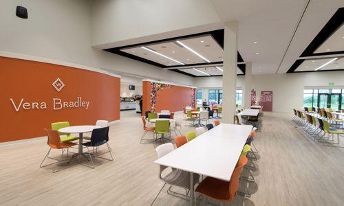 Bright, modern café interior with orange wall, white tables, colorful chairs, and ample natural light, fostering a lively atmosphere.