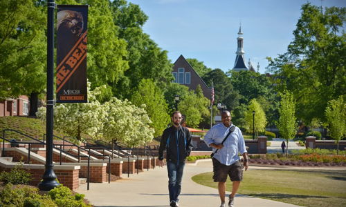 Two individuals walk a sunny path among greenery, enjoying friendship and leisure in a cheerful, tranquil setting.