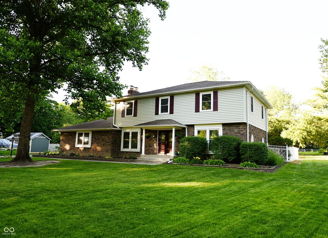 Two-story house with brick and siding in a lush yard, surrounded by trees, conveys warmth, tranquility, and a sense of home.
