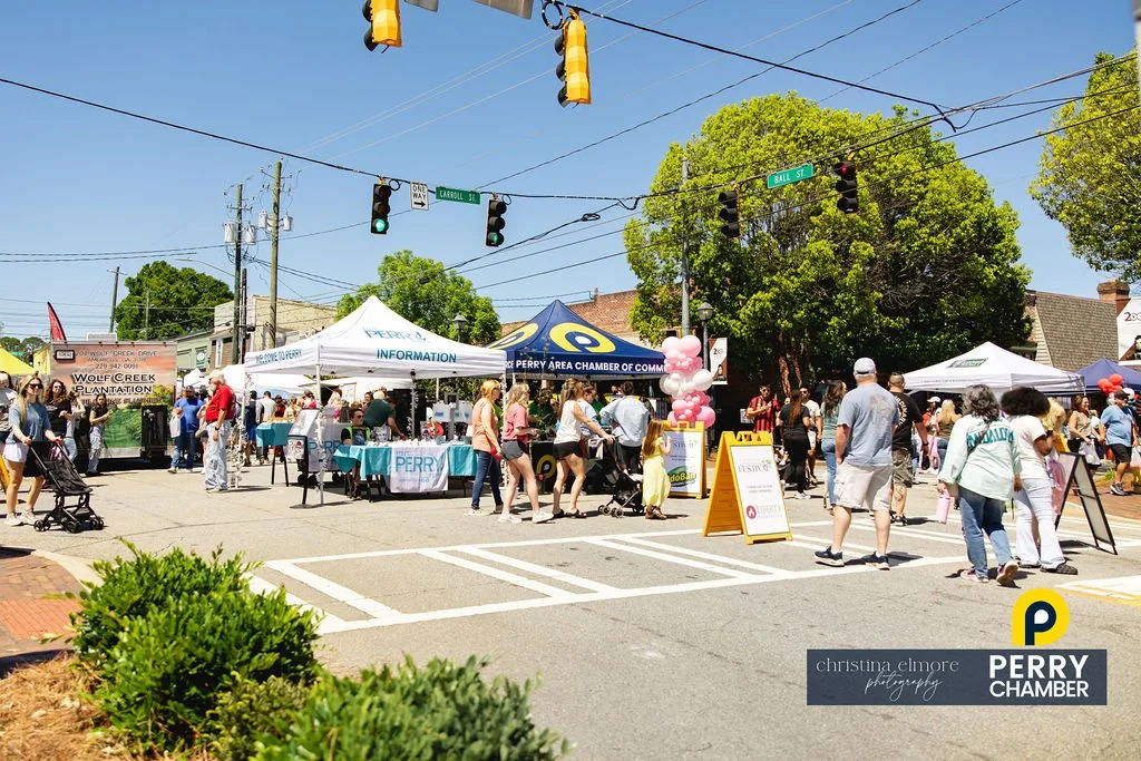 Lively street scene at a community festival with tents, crowds, joy, and inclusivity, all under a bright, sunny sky.