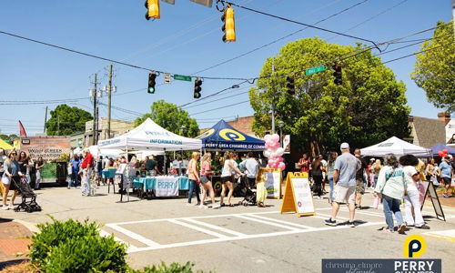 Lively street scene at a community festival with tents, crowds, joy, and inclusivity, all under a bright, sunny sky.