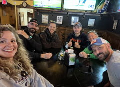 A cheerful group of people at a casual gathering, smiles and relaxed vibes in a warm, inviting pub setting.
