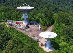 Two large satellite dishes in a lush, green landscape depict the harmony of technology and nature, evoking curiosity and contemplation.