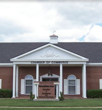 A classic brick building with columns houses the Chamber of Commerce, surrounded by flags and a well-maintained landscape.