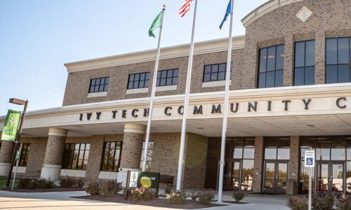 Ivy Tech Community College entrance with modern brick and glass, flags, signage, greenery, and a welcoming atmosphere.
