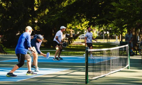 An outdoor pickleball game with four engaged players, showcasing energy, enthusiasm, and a vibrant park setting.