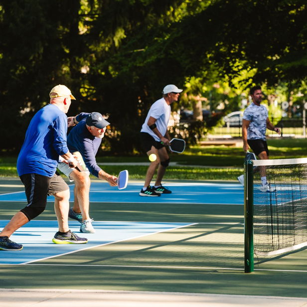 An outdoor pickleball game with four engaged players, showcasing energy, enthusiasm, and a vibrant park setting.