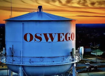 Water tower with "OSWEGO" in red letters against a vibrant sunset sky, evoking nostalgia and community warmth.