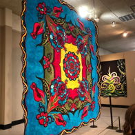 Vibrant textile artwork with bold colors and intricate floral patterns evokes joy and celebration in an exhibition space.