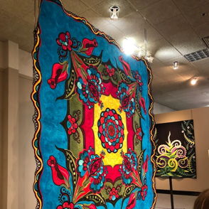 Vibrant textile artwork with bold colors and intricate floral patterns evokes joy and celebration in an exhibition space.