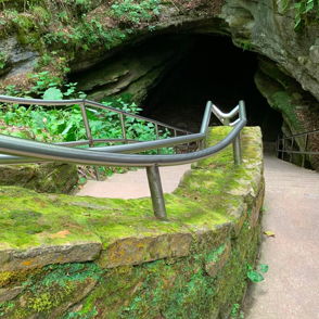 Pathway leading to a dark, inviting cave entrance, surrounded by lush greenery and mossy rocks, evokes mystery and adventure.