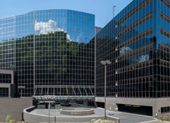 Modern urban building with a sleek glass facade, reflecting clouds and greenery, evoking professionalism and optimism.