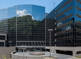 Modern urban building with a sleek glass facade, reflecting clouds and greenery, evoking professionalism and optimism.