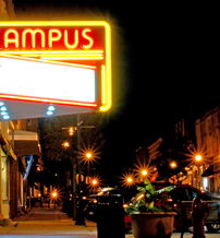 Vibrant nighttime street scene with a retro neon "CAMPUS" sign, evoking nostalgia, warmth, and a lively community atmosphere.