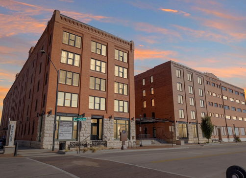 A pair of multistory brick buildings at sunset, blending historic and modern styles, evoke warmth, nostalgia, and community.