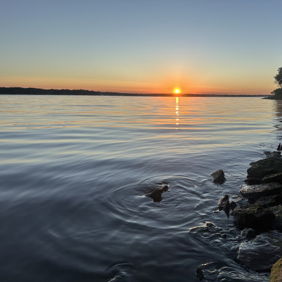Serene lakeside scene at sunset; vibrant colors reflect on calm water, evoking tranquility and introspection.