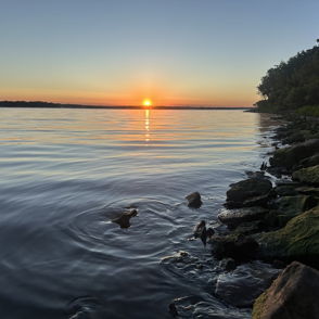 Serene lakeside scene at sunset; vibrant colors reflect on calm water, evoking tranquility and introspection.