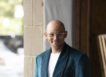 Person in a teal blazer stands confidently in an unfinished building, evoking a creative, dynamic atmosphere.