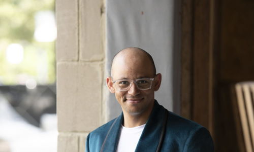 Person in a teal blazer stands confidently in an unfinished building, evoking a creative, dynamic atmosphere.