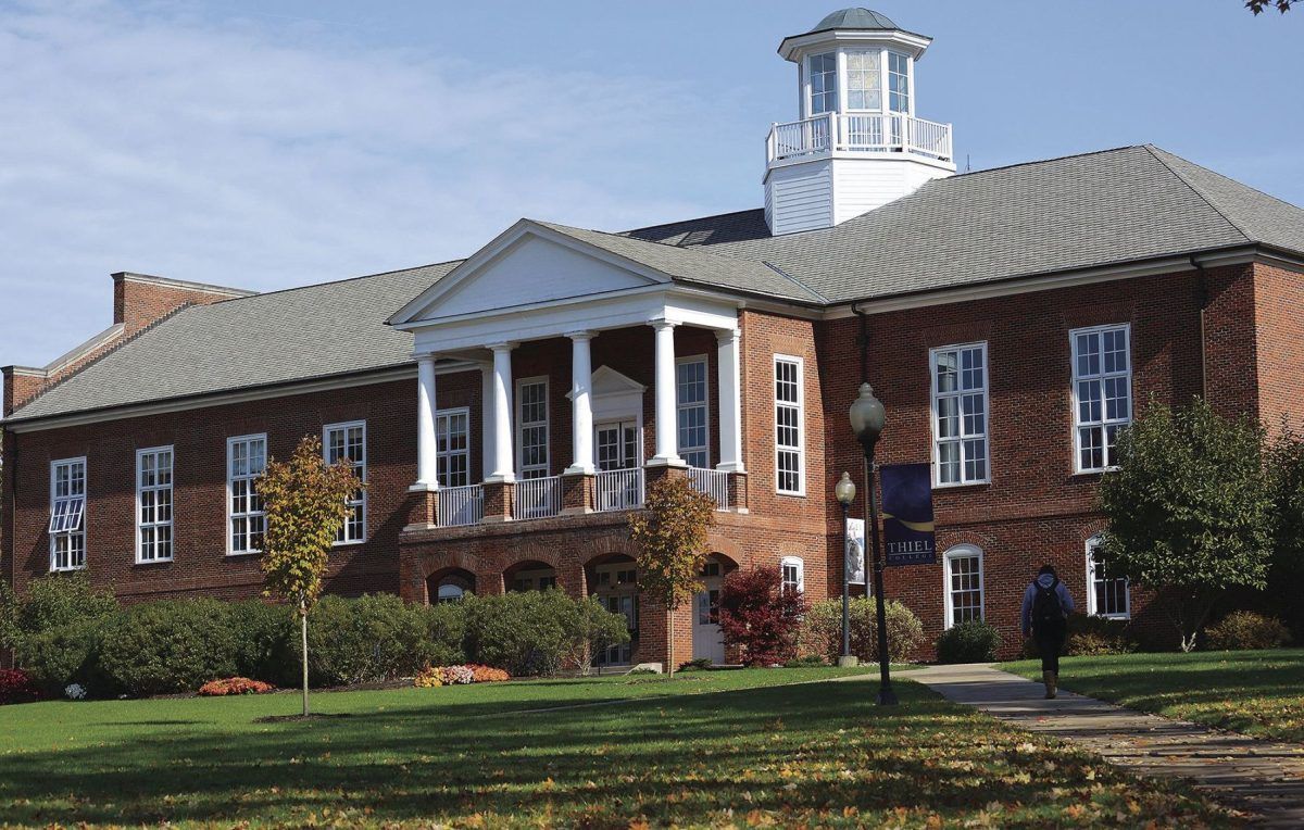 A stately brick building with columns and a cupola, set in vibrant, well-landscaped surroundings on a clear day.