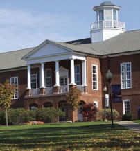 A stately brick building with columns and a cupola, set in vibrant, well-landscaped surroundings on a clear day.