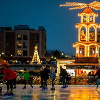 Outdoor ice skating rink with skaters, illuminated carousel-like pavilion, festive lights, and a Christmas tree, evoking joy.