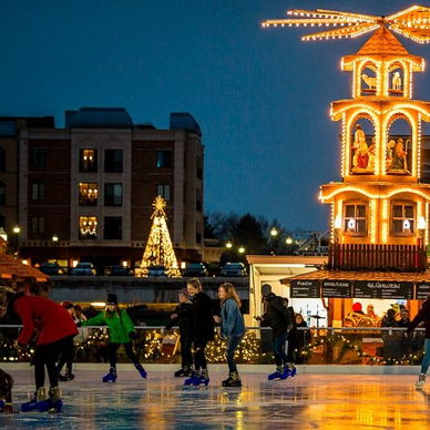 Outdoor ice skating rink with skaters, illuminated carousel-like pavilion, festive lights, and a Christmas tree, evoking joy.