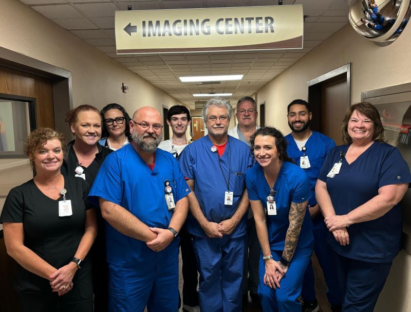 Group of smiling healthcare professionals in blue scrubs by an Imaging Center sign, reflecting teamwork and care.