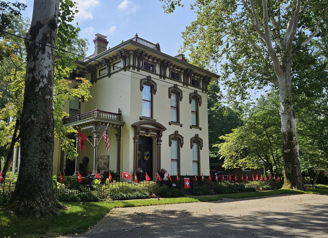 Historic Victorian home with ornate details, surrounded by greenery and flags, evoking nostalgia and a festive atmosphere.