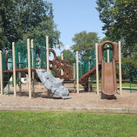 Playground with slides and climbing structures amidst green trees and blue sky, evoking joy and nostalgia for childhood fun.