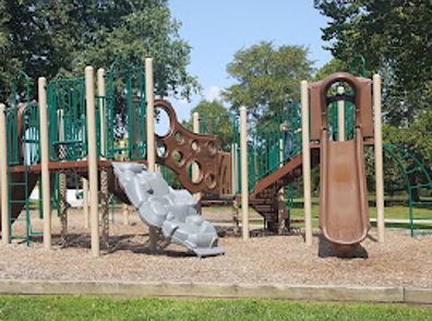 Playground with slides and climbing structures amidst green trees and blue sky, evoking joy and nostalgia for childhood fun.