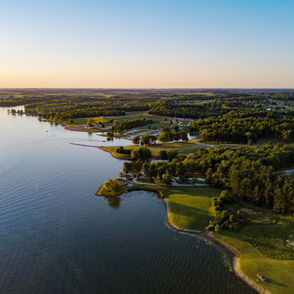 Serene landscape with a calm lake, lush greenery, hills, and a soft orange-blue sky, evoking peace and tranquility.