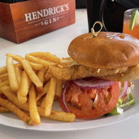 A mouthwatering sandwich with a crispy fillet, fresh veggies, French fries, and a drink, evoking comfort and indulgence.