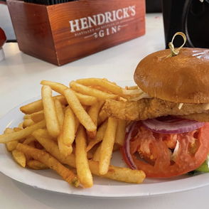 A mouthwatering sandwich with a crispy fillet, fresh veggies, French fries, and a drink, evoking comfort and indulgence.