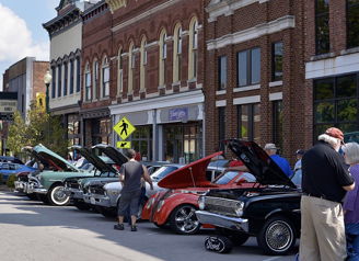 A vibrant parade of classic cars on a quaint street, with crowds celebrating community and automotive history.