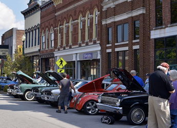 A vibrant parade of classic cars on a quaint street, with crowds celebrating community and automotive history.