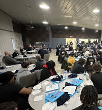 Attendees engaged in a conference, seated at circular tables, focused on discussions in a collaborative atmosphere.