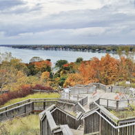 Scenic view from above a lake, framed by vibrant autumn foliage, wooden steps lead to a tranquil, colorful landscape.