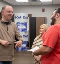 Three smiling people converse in a relaxed, professional setting, radiating joy and camaraderie.