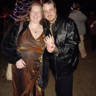 Two individuals happily posing together in festive attire, surrounded by colorful lights, conveying joy and celebration.