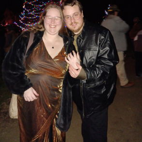 Two individuals happily posing together in festive attire, surrounded by colorful lights, conveying joy and celebration.