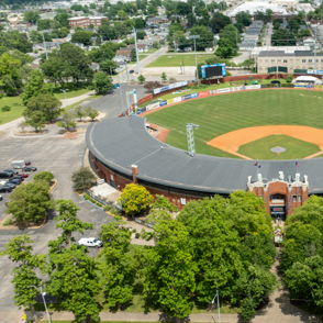 Aerial view of a baseball stadium amidst greenery and urban landscape, evoking nostalgia and community spirit of the game.
