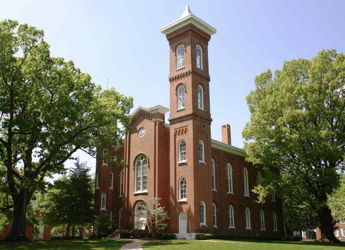 Historic brick building with a bell tower, surrounded by trees under a blue sky, evoking peace and nostalgia.