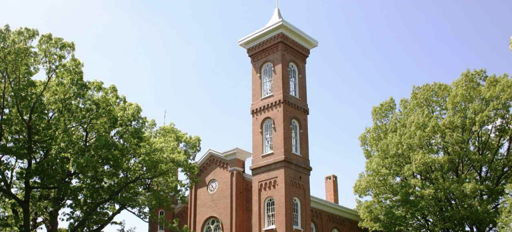 Historic brick building with a bell tower, surrounded by trees under a blue sky, evoking peace and nostalgia.