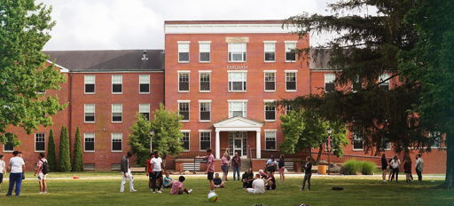 A lively outdoor scene near a brick building, with children and young adults playing and socializing in a cheerful atmosphere.