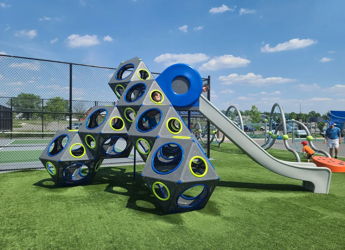Colorful modern playground with geometric climbing frame, slide, and synthetic grass. Bright day sky enhances playful mood.